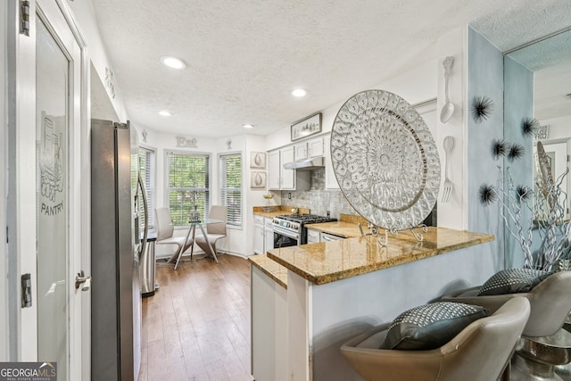 4467 Pineridge Cir, Atlanta, GA 30338 - kitchen featuring appliances with stainless steel finishes, a textured ceiling, a peninsula, under cabinet range hood, and light stone countertops