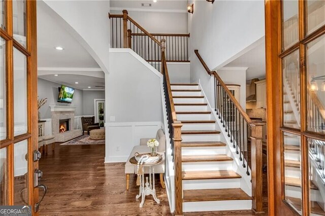 5301 Regency Lake Ct, Sugar Hill, GA 30518 - stairs featuring a high ceiling, wood finished floors, a warm lit fireplace, ornamental molding, and a wainscoted wall