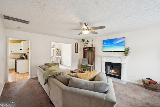 5686 Grindstone Dr, Buford, GA 30518 - living area with light carpet, ceiling fan, a glass covered fireplace, and a textured ceiling