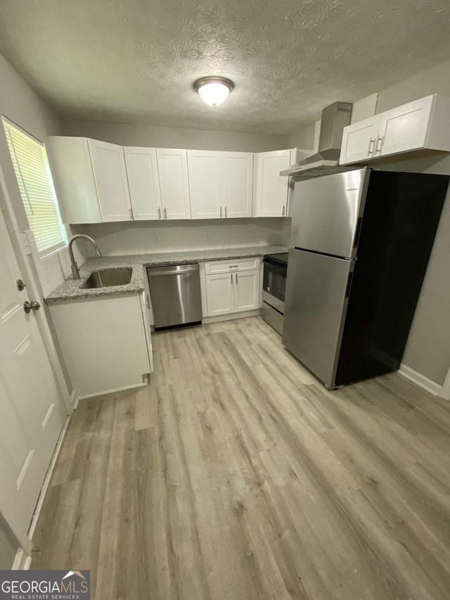 3351 Fox St, Duluth, GA 30096 - kitchen featuring appliances with stainless steel finishes, wall chimney exhaust hood, light wood finished floors, white cabinets, and a textured ceiling