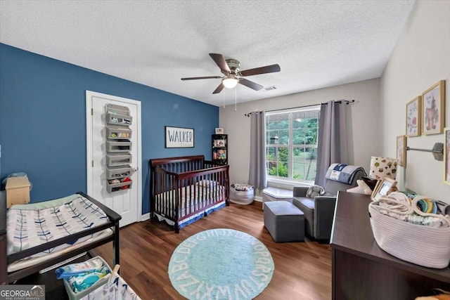 1050 Birdseye Vw, Locust Grove, GA 30248 - bedroom featuring a textured ceiling, wood finished floors, a crib, and ceiling fan