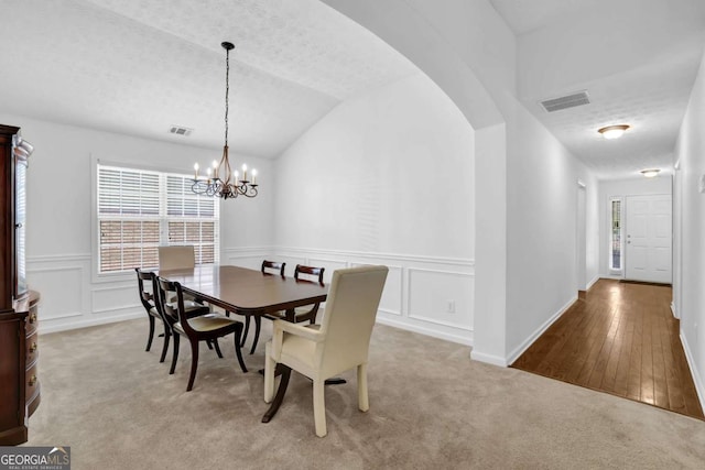 5565 Ashmoore Ct, Flowery Branch, GA 30542 - carpeted dining room featuring a chandelier, vaulted ceiling, a decorative wall, wainscoting, and arched walkways