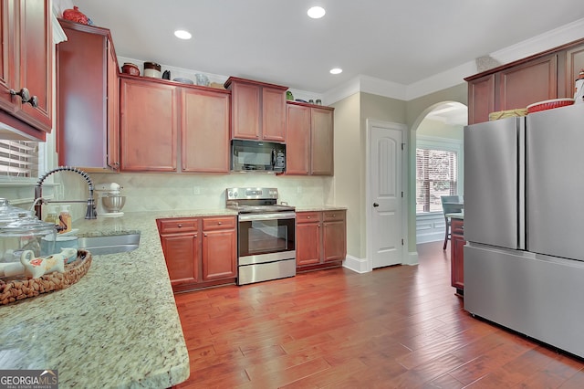 108 Village Pl, Newnan, GA 30265 - kitchen with stainless steel appliances, arched walkways, light stone counters, backsplash, and wood finished floors
