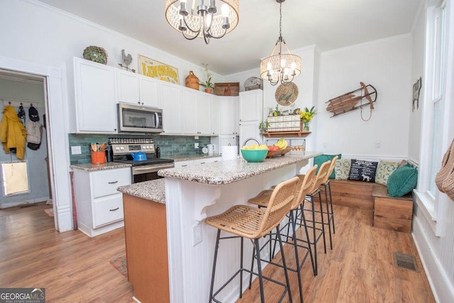 202 E Oak St, Luthersville, GA 30251 - kitchen with stainless steel appliances, a chandelier, a kitchen breakfast bar, backsplash, and light wood finished floors