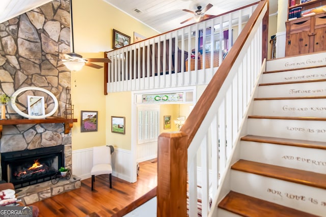 705 Laurel Ridge Dr, Ellijay, GA 30536 - staircase with a ceiling fan, wood finished floors, a wainscoted wall, a stone fireplace, and a high ceiling