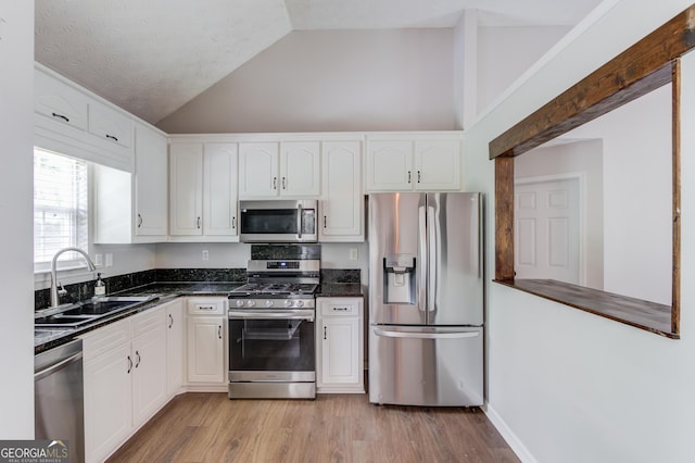 926 Masters Dr, Monroe, GA 30655 - kitchen featuring appliances with stainless steel finishes, lofted ceiling, white cabinetry, light wood-type flooring, and dark stone counters