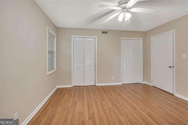 122 S Island Square Dr, Saint Simons, GA 31522 - unfurnished bedroom with two closets, light wood-style flooring, a textured ceiling, and a ceiling fan