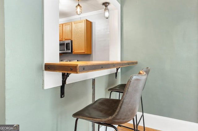 960 Taft Ave NE Unit 9, Atlanta, GA 30309 - kitchen with stainless steel microwave, crown molding, a breakfast bar area, and light brown cabinetry