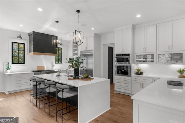 4451 Shellie Ln, Oakwood, GA 30566 - kitchen with exhaust hood, stainless steel appliances, an island with sink, a kitchen bar, and light countertops