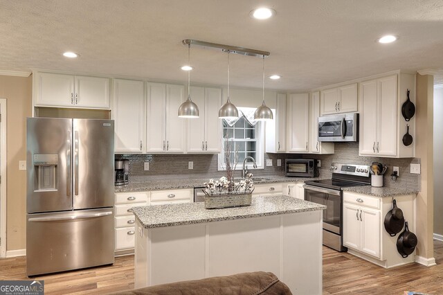 241 Lavern Ct, Winder, GA 30680 - kitchen with appliances with stainless steel finishes, white cabinetry, a kitchen island, light wood finished floors, and backsplash