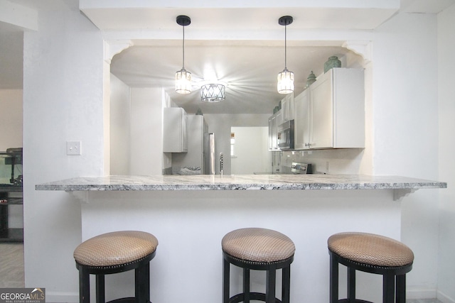 711 Main St, Byron, GA 31008 - kitchen featuring stainless steel microwave, a peninsula, white cabinets, a breakfast bar, and pendant lighting