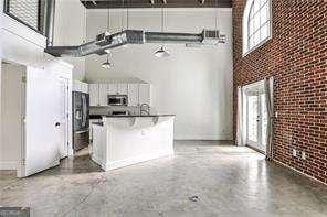 791 Wylie St SE Unit 404, Atlanta, GA 30316 - kitchen featuring a towering ceiling, stainless steel microwave, brick wall, freestanding refrigerator, and concrete flooring