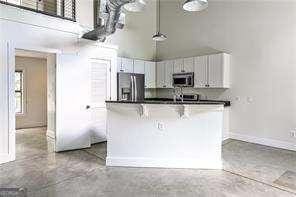 791 Wylie St SE Unit 404, Atlanta, GA 30316 - kitchen with appliances with stainless steel finishes, dark countertops, a towering ceiling, a kitchen breakfast bar, and decorative light fixtures