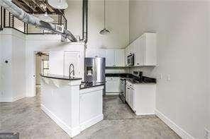 791 Wylie St SE Unit 404, Atlanta, GA 30316 - kitchen with concrete floors, stainless steel microwave, dark countertops, white cabinetry, and a towering ceiling