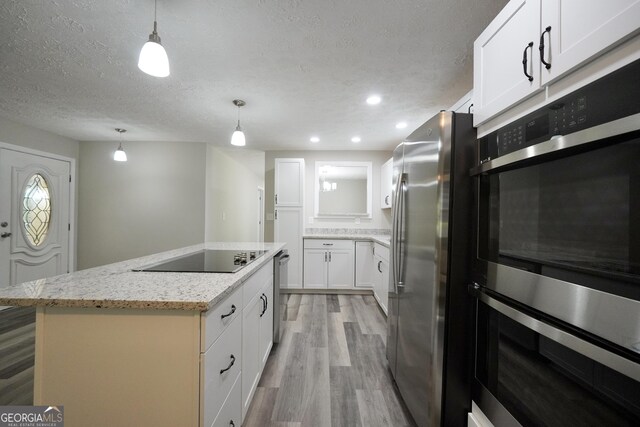 118 Turtle Cove Trwy, Monticello, GA 31064 - kitchen featuring appliances with stainless steel finishes, a textured ceiling, light wood-type flooring, a center island, and light stone countertops