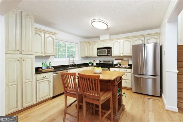 9685 Cone Ct, Roswell, GA 30075 - kitchen featuring stainless steel appliances, cream cabinetry, light wood finished floors, and a textured ceiling