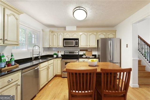 9685 Cone Ct, Roswell, GA 30075 - kitchen with stainless steel appliances, cream cabinets, light wood-type flooring, dark countertops, and a textured ceiling
