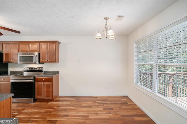 40 Browning Dr, Covington, GA 30016 - kitchen featuring appliances with stainless steel finishes, brown cabinetry, light wood finished floors, a chandelier, and dark countertops