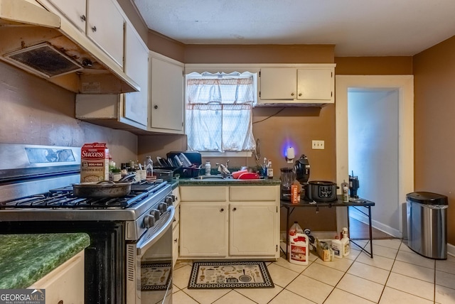 1115 W 51st St, Savannah, GA 31405 - kitchen featuring stainless steel range with gas stovetop, under cabinet range hood, light tile patterned flooring, dark countertops, and white cabinetry