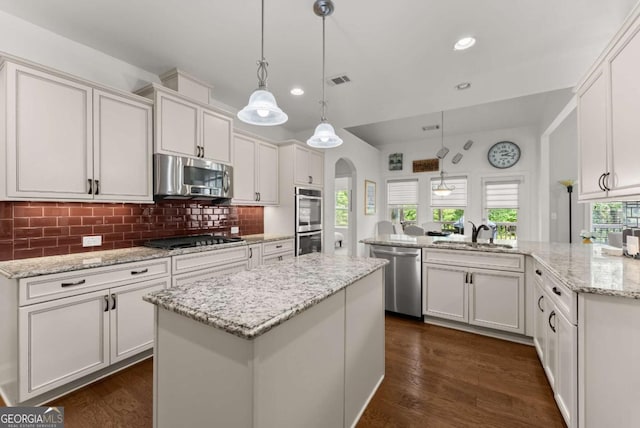 6460 Valley Crossing Way, Cumming, GA 30028 - kitchen with appliances with stainless steel finishes, a kitchen island, arched walkways, white cabinetry, and tasteful backsplash