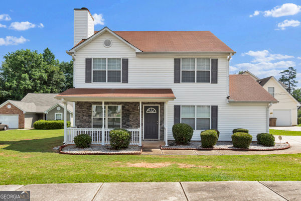 7770 Hana Ct, Jonesboro, GA 30236 - traditional-style house featuring covered porch, a front yard, a chimney, a garage, and a shingled roof