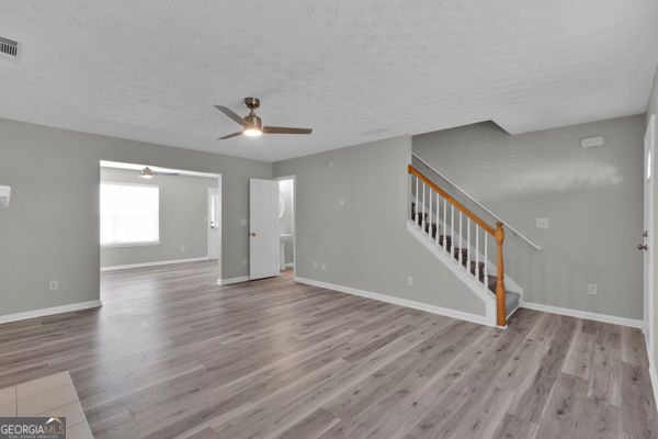 7770 Hana Ct, Jonesboro, GA 30236 - unfurnished living room with a ceiling fan, wood finished floors, stairs, and a textured ceiling