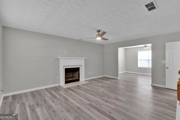 7770 Hana Ct, Jonesboro, GA 30236 - unfurnished living room with ceiling fan, a fireplace with flush hearth, wood finished floors, and a textured ceiling