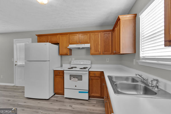 7770 Hana Ct, Jonesboro, GA 30236 - kitchen featuring white appliances, under cabinet range hood, brown cabinets, light countertops, and light wood-style flooring