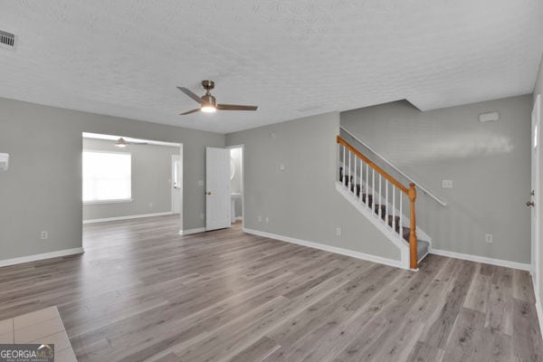 7770 Hana Ct, Jonesboro, GA 30236 - unfurnished living room with a ceiling fan, wood finished floors, stairs, and a textured ceiling