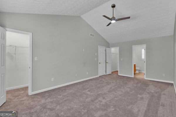 7770 Hana Ct, Jonesboro, GA 30236 - unfurnished bedroom with a walk in closet, a closet, carpet, connected bathroom, and high vaulted ceiling