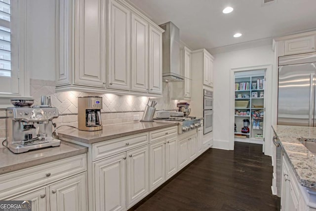3467 Brookleigh Ln NE, Atlanta, GA 30319 - kitchen with wall chimney range hood, stainless steel appliances, white cabinetry, dark wood-style flooring, and decorative backsplash