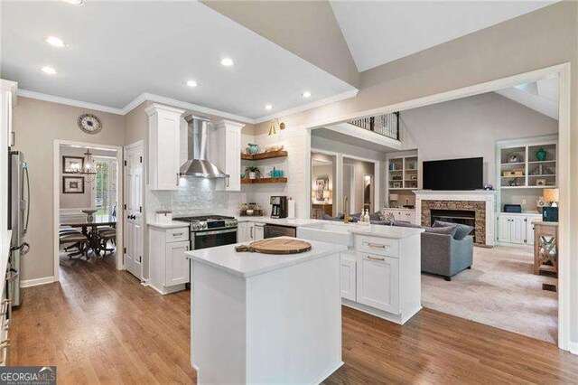 501 Avery Creek Pointe, Woodstock, GA 30188 - kitchen with wall chimney range hood, stainless steel gas stove, a peninsula, lofted ceiling, and crown molding