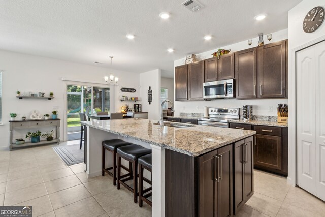 159 College St, Kingsland, GA 31548 - kitchen with stainless steel appliances, a chandelier, light tile patterned flooring, a kitchen bar, and dark brown cabinetry