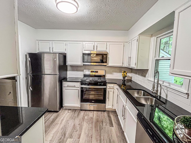3150 Stratford Green Pl, Avondale Estates, GA 30002 - kitchen featuring appliances with stainless steel finishes, light wood-style flooring, washer / clothes dryer, a textured ceiling, and white cabinetry