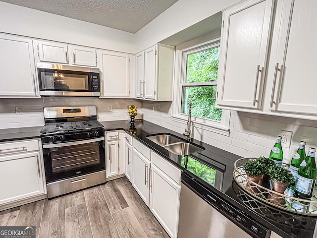 3150 Stratford Green Pl, Avondale Estates, GA 30002 - kitchen featuring stainless steel appliances, dark countertops, light wood finished floors, white cabinets, and a textured ceiling