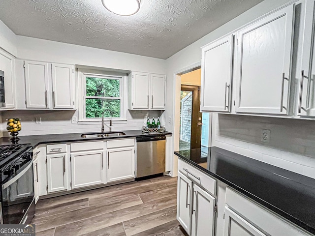 3150 Stratford Green Pl, Avondale Estates, GA 30002 - kitchen featuring appliances with stainless steel finishes, dark countertops, light wood-type flooring, white cabinetry, and a textured ceiling