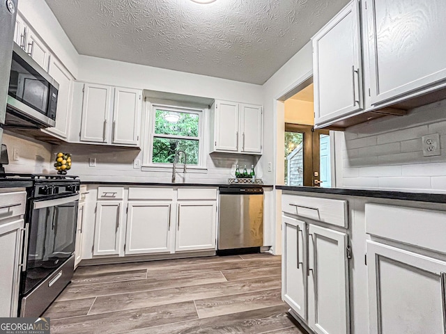 3150 Stratford Green Pl, Avondale Estates, GA 30002 - kitchen with stainless steel appliances, light wood-type flooring, white cabinetry, tasteful backsplash, and a textured ceiling