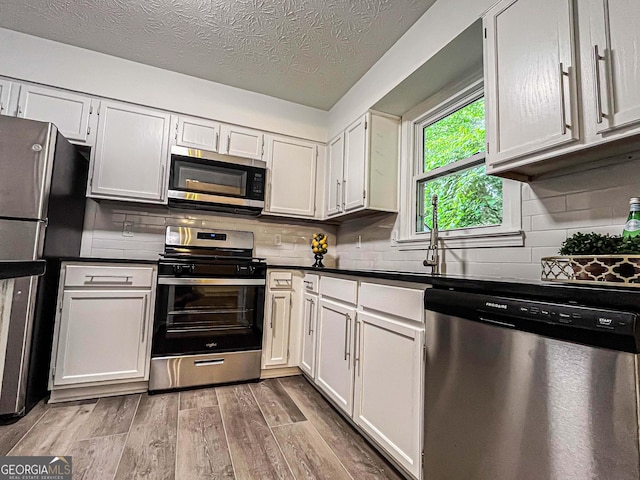 3150 Stratford Green Pl, Avondale Estates, GA 30002 - kitchen with stainless steel appliances, light wood-style flooring, dark countertops, backsplash, and a textured ceiling