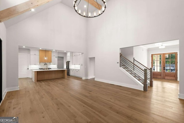 6750 Pannell Rd, Buford, GA 30518 - unfurnished living room with a chandelier, light wood-style flooring, high vaulted ceiling, stairway, and french doors