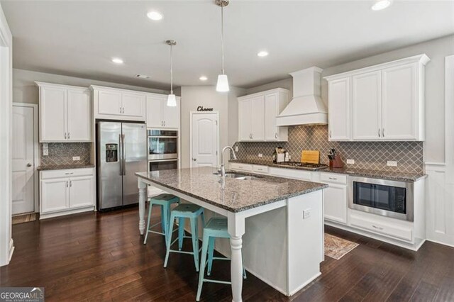 62 Saint Ives Cir, Winder, GA 30680 - kitchen featuring stainless steel appliances, custom range hood, tasteful backsplash, a breakfast bar, and white cabinets