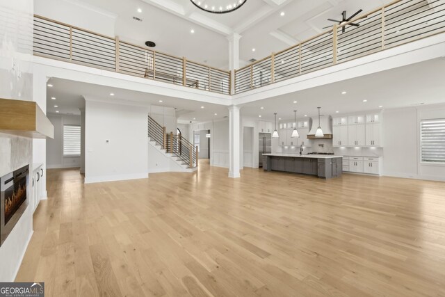 3735 Hamilton Mill Rd, Buford, GA 30519 - unfurnished living room featuring a high ceiling, decorative columns, a tile fireplace, ceiling fan, and light wood-style floors