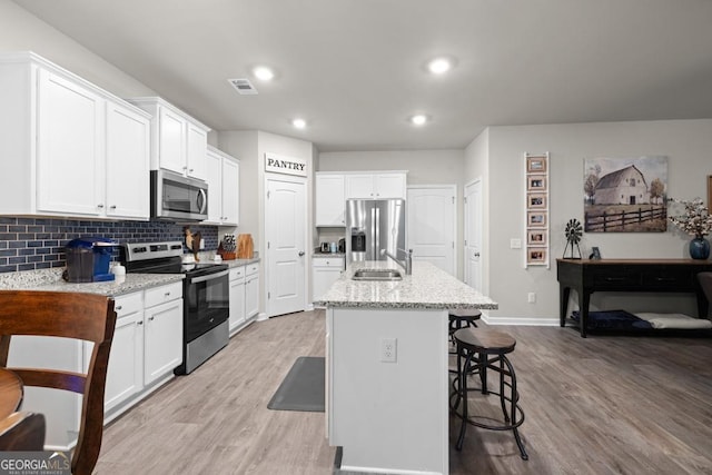 2046 Westbrook Rd, Commerce, GA 30530 - kitchen featuring stainless steel appliances, light wood-style flooring, white cabinets, backsplash, and a breakfast bar