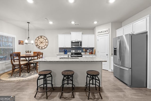 2046 Westbrook Rd, Commerce, GA 30530 - kitchen featuring appliances with stainless steel finishes, white cabinets, light wood-style floors, a kitchen island with sink, and backsplash