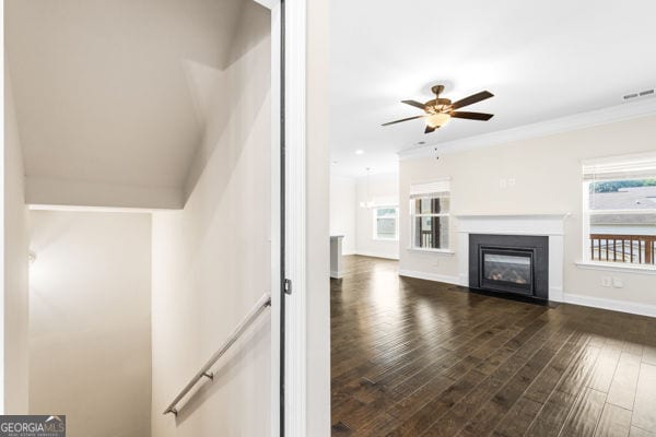 1494 Weeping Tree Cir, Hoschton, GA 30548 - unfurnished living room with healthy amount of natural light, a ceiling fan, dark wood-style flooring, a fireplace with flush hearth, and crown molding