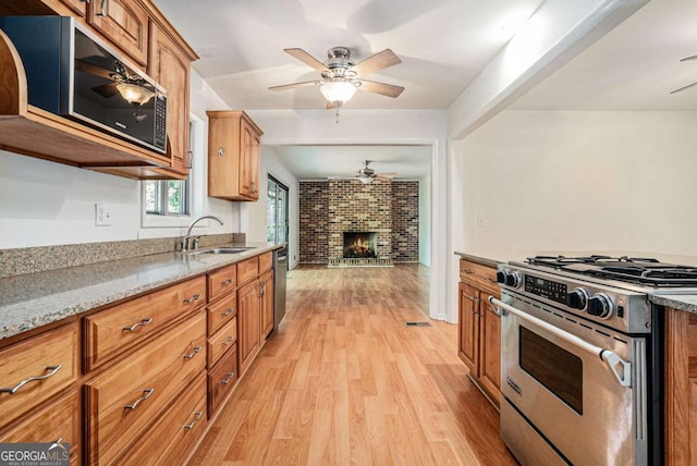 1260 Fork Creek Trl, Decatur, GA 30033 - kitchen featuring appliances with stainless steel finishes, a ceiling fan, light wood-style floors, a brick fireplace, and brown cabinetry
