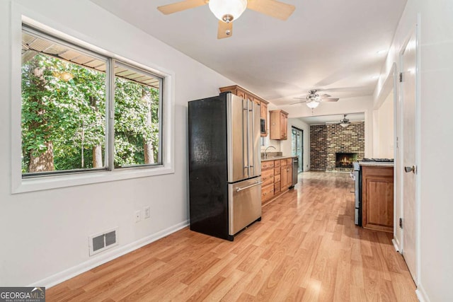 1260 Fork Creek Trl, Decatur, GA 30033 - kitchen with appliances with stainless steel finishes, a ceiling fan, a brick fireplace, light wood-type flooring, and brown cabinetry