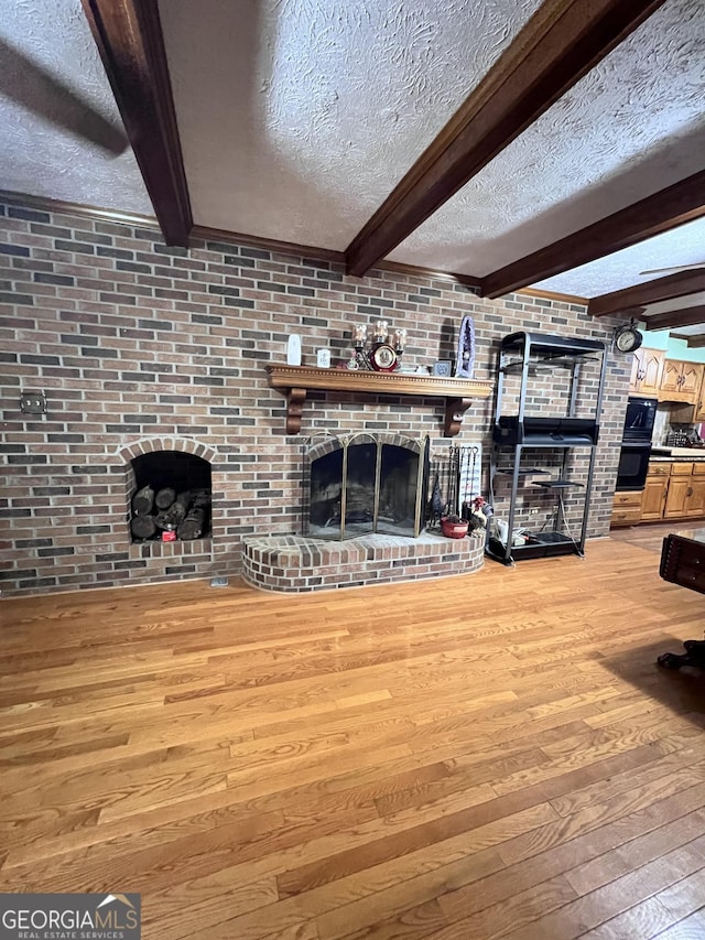 186 Kingston Rd, Colbert, GA 30628 - unfurnished living room with a brick fireplace, light wood-type flooring, a textured ceiling, and beam ceiling