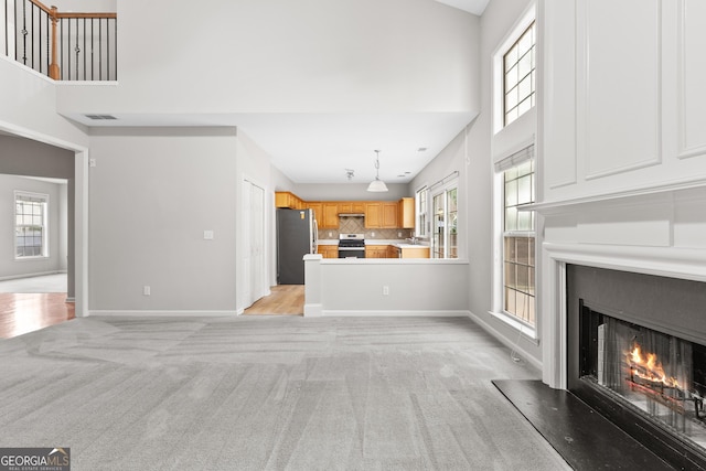 8750 Redford Ln, Suwanee, GA 30024 - unfurnished living room with a towering ceiling, light colored carpet, a warm lit fireplace, and healthy amount of natural light
