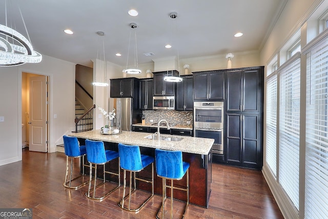 1306 Harris Way, Brookhaven, GA 30319 - kitchen featuring appliances with stainless steel finishes, a kitchen island with sink, backsplash, dark cabinetry, and a kitchen breakfast bar