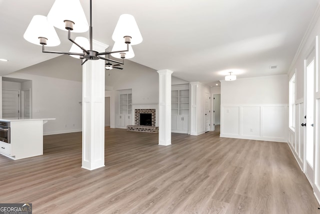 797 Ode Peppers Rd, Winder, GA 30680 - unfurnished living room with a chandelier, a brick fireplace, vaulted ceiling, light wood finished floors, and ornate columns
